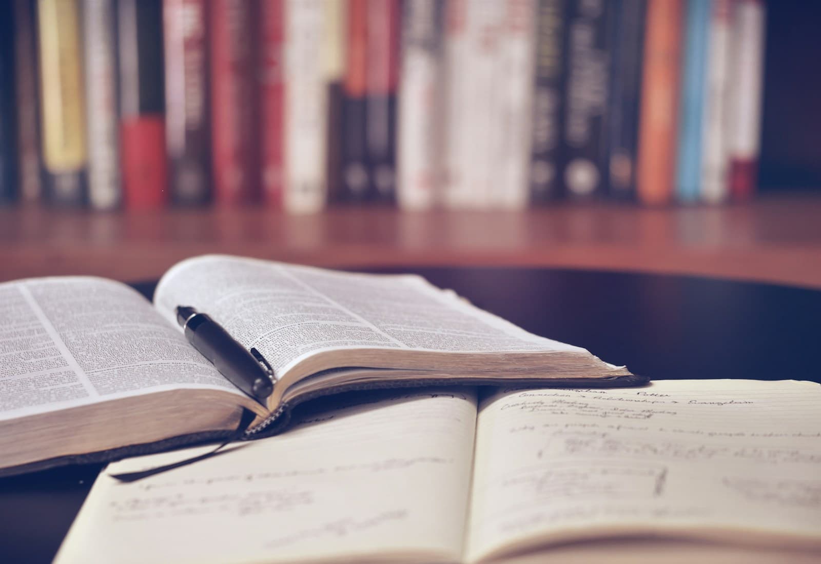 Open study books and a handwritten notebook in front of a library shelf.