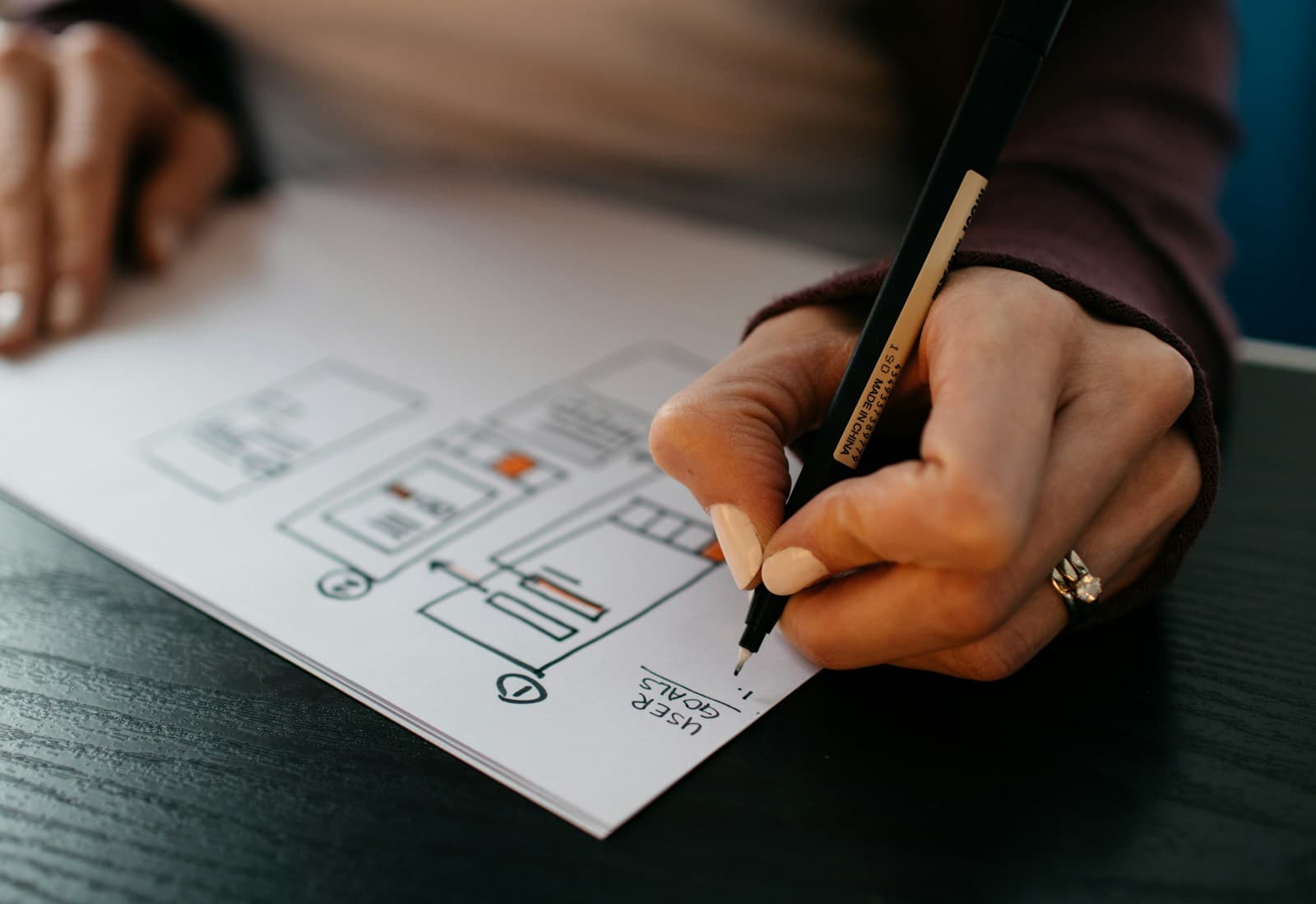 Hand sketching a user-interface wireframe with a fine pen on paper.